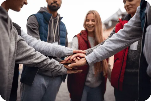 Grupo de pessoas unindo as mãos no centro, simbolizando trabalho em equipe e união em um contexto de colaboração comunitária.