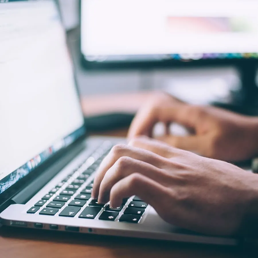 Uma pessoa digitando em um laptop, foco nas mãos sobre o teclado. O fundo é desfocado.